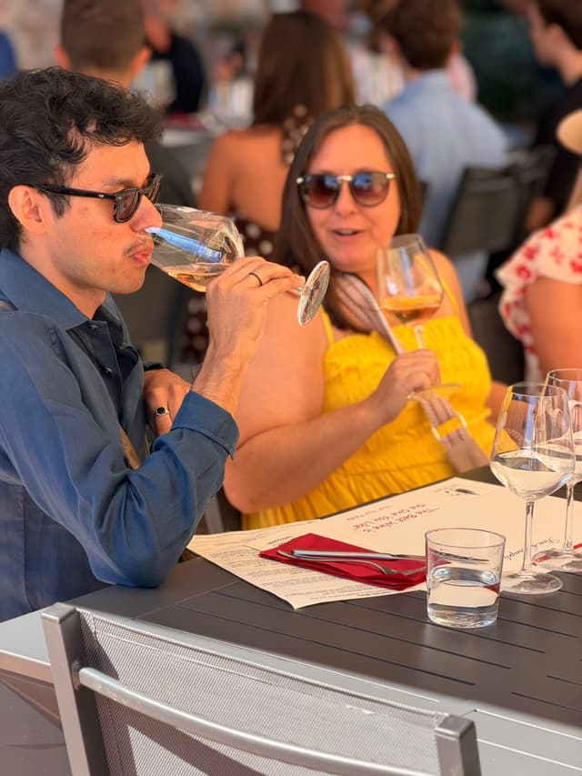 Two guests tasting white wine at a shaded outdoor table in the Tuscan countryside