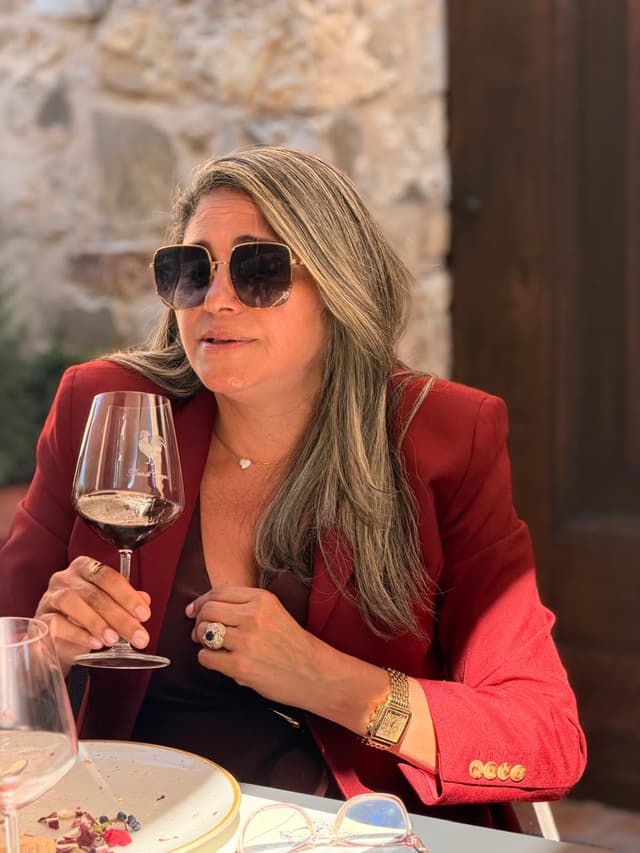 Guest with a glass of red wine in front of the old stone wall of the wine estate