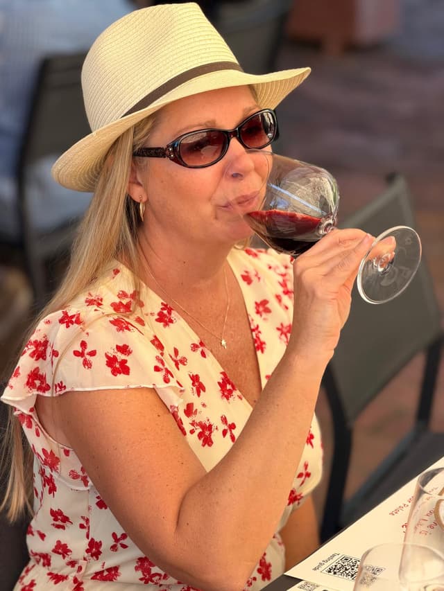 Guest in a straw hat sipping red wine at the tasting table in the late afternoon sun
