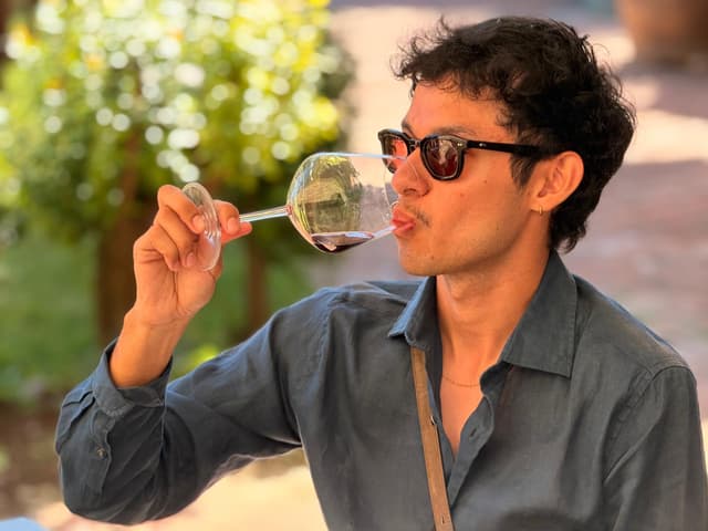 Guest sipping red wine outdoors, the estate garden out of focus behind